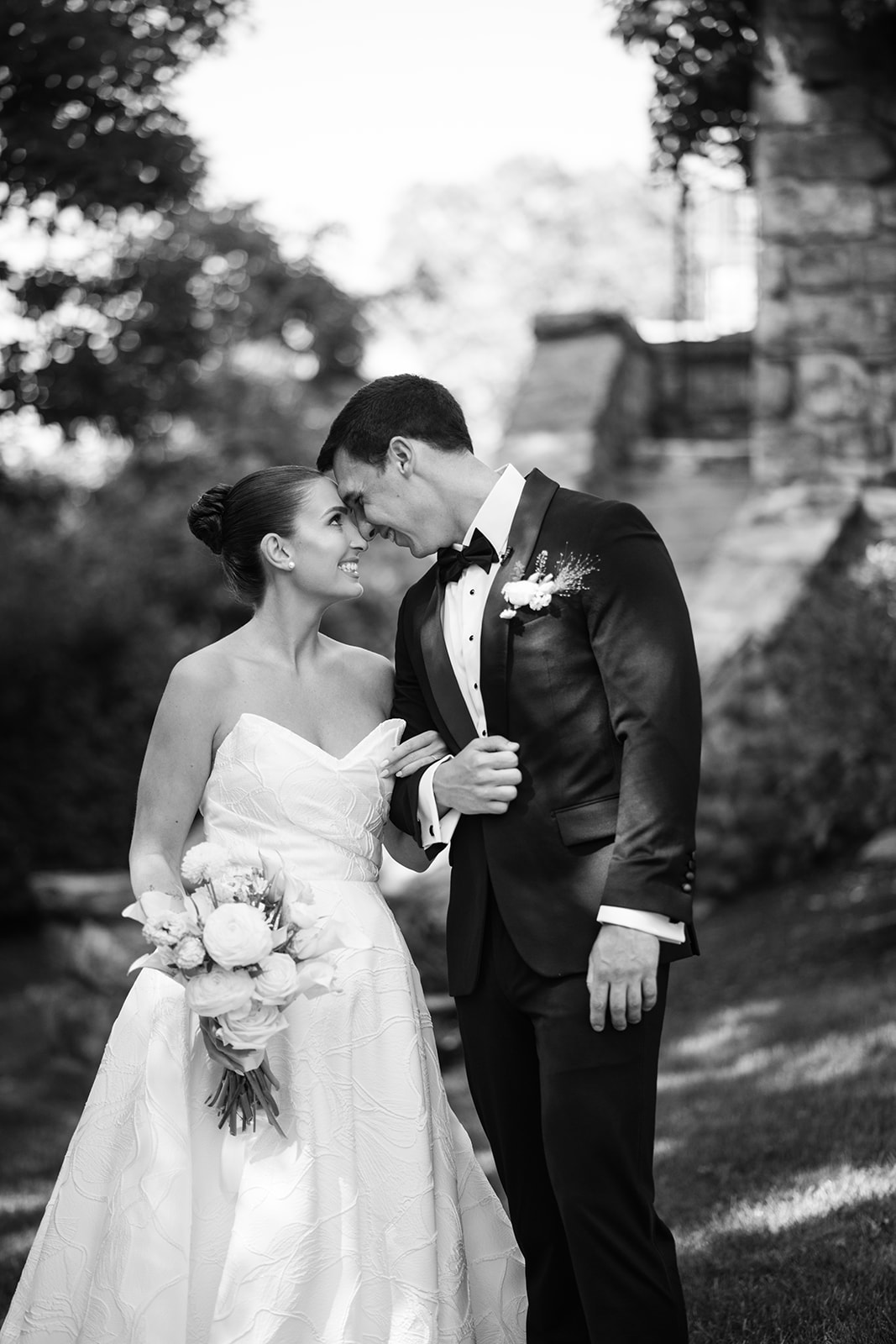 Black and white film photo of the bride and groom touching foreheads and laughing happily outside.